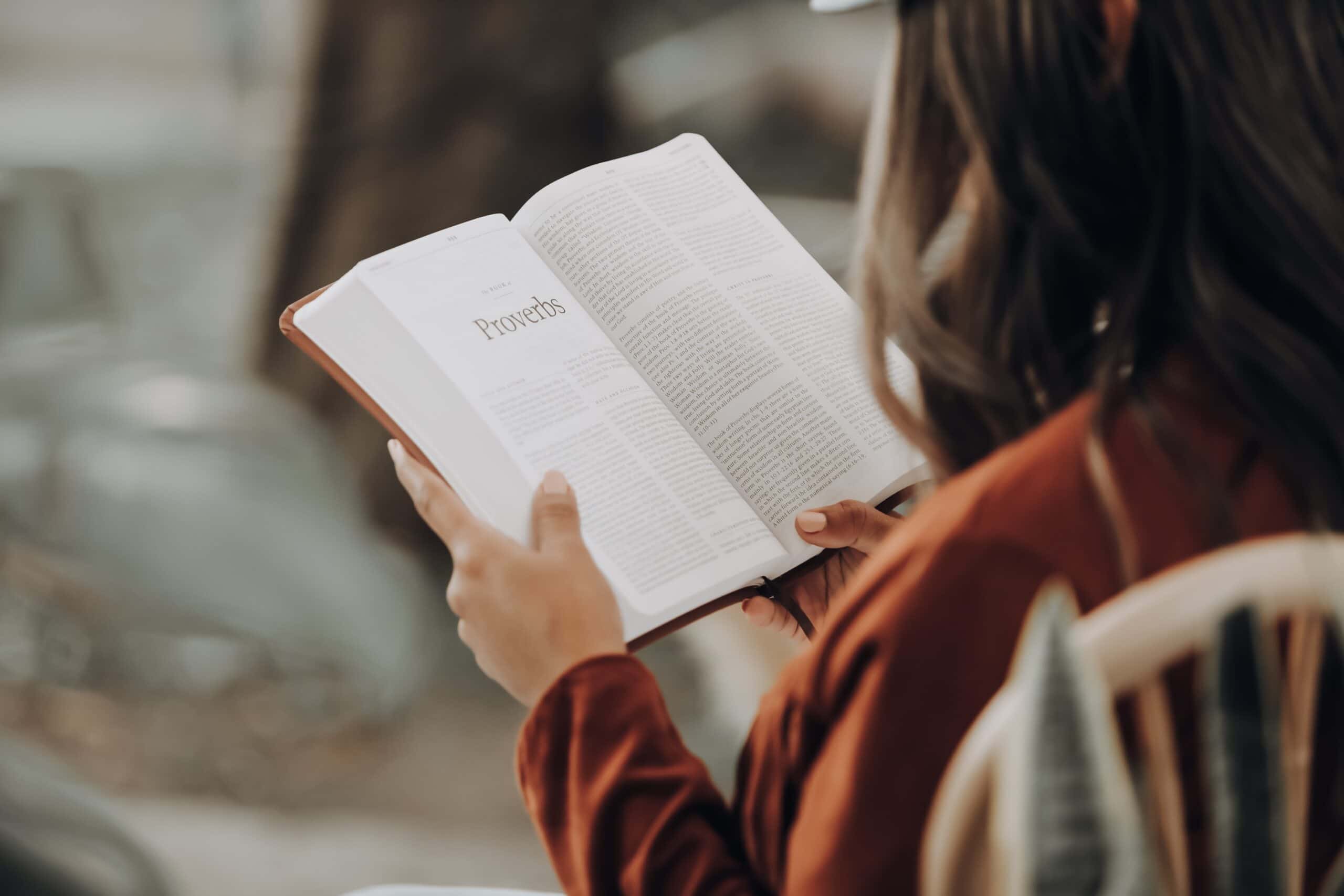 girl in brown sweater sitting in a chair holding and reading a Bible