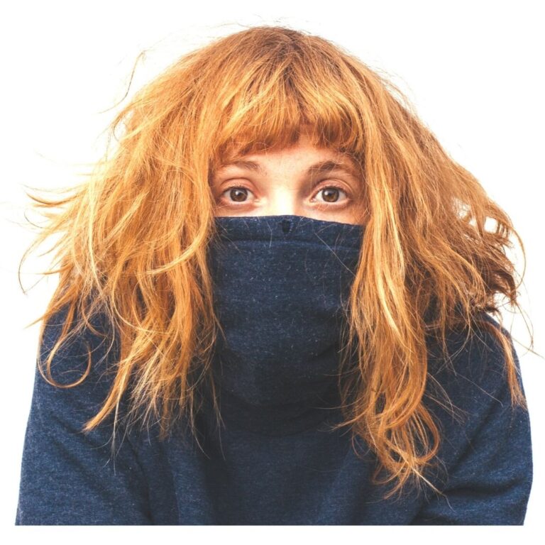 a red headed girl in a black turtleneck shirt with the neck pulled up over her chin and nose and nervous eyes.